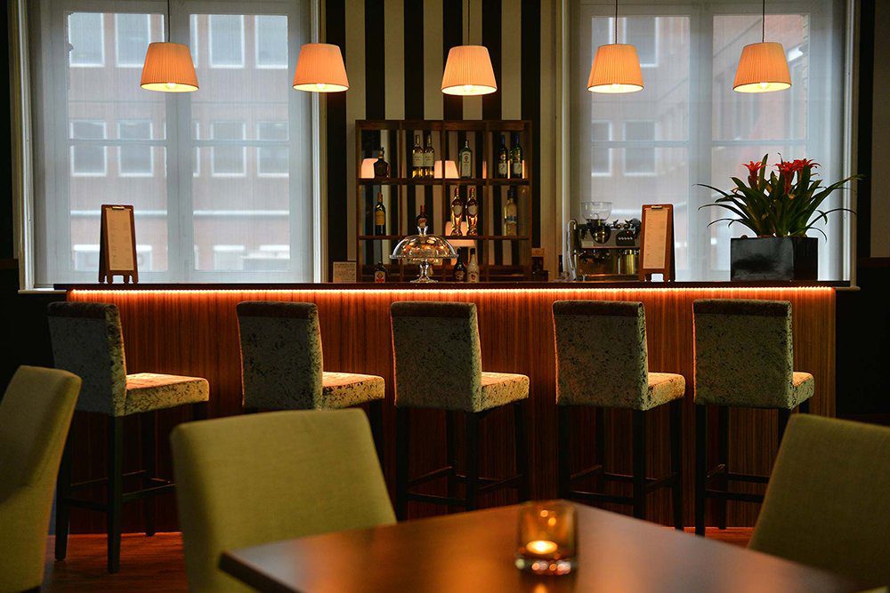 A dimly lit room showing a number of tall velvet stools lined up along a bar with suspended lighting along it.