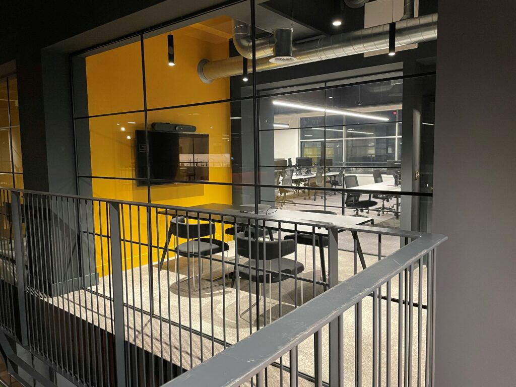 A photo from the balcony inside Beevers and Struthers. The photo is of a meeting room with glass exterior walls, a yellow back wall and table and chairs inside.