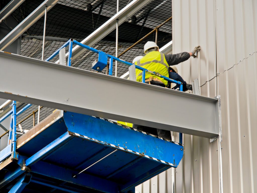 A photo of a man in construction appropriate PPE on a cherry picker looking at cladding on the side of a building.