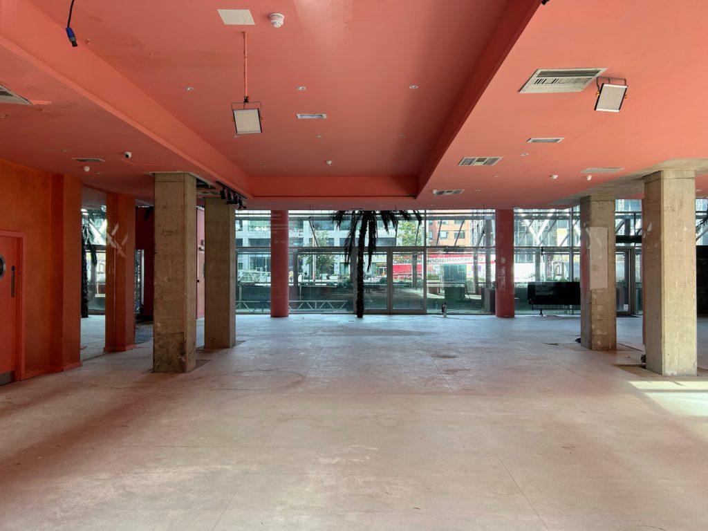 View of an empty restaurant building featuring a concrete floor, concrete pillars and terracotta coloured ceiling.