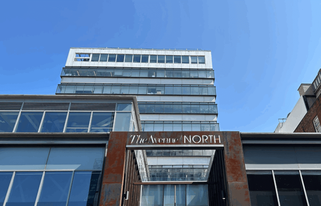 Cladding and glass facade of a 12 storey commercial building behind a Corten steel archway with the lettering: The Avenue/ NORTH cut into the steel.