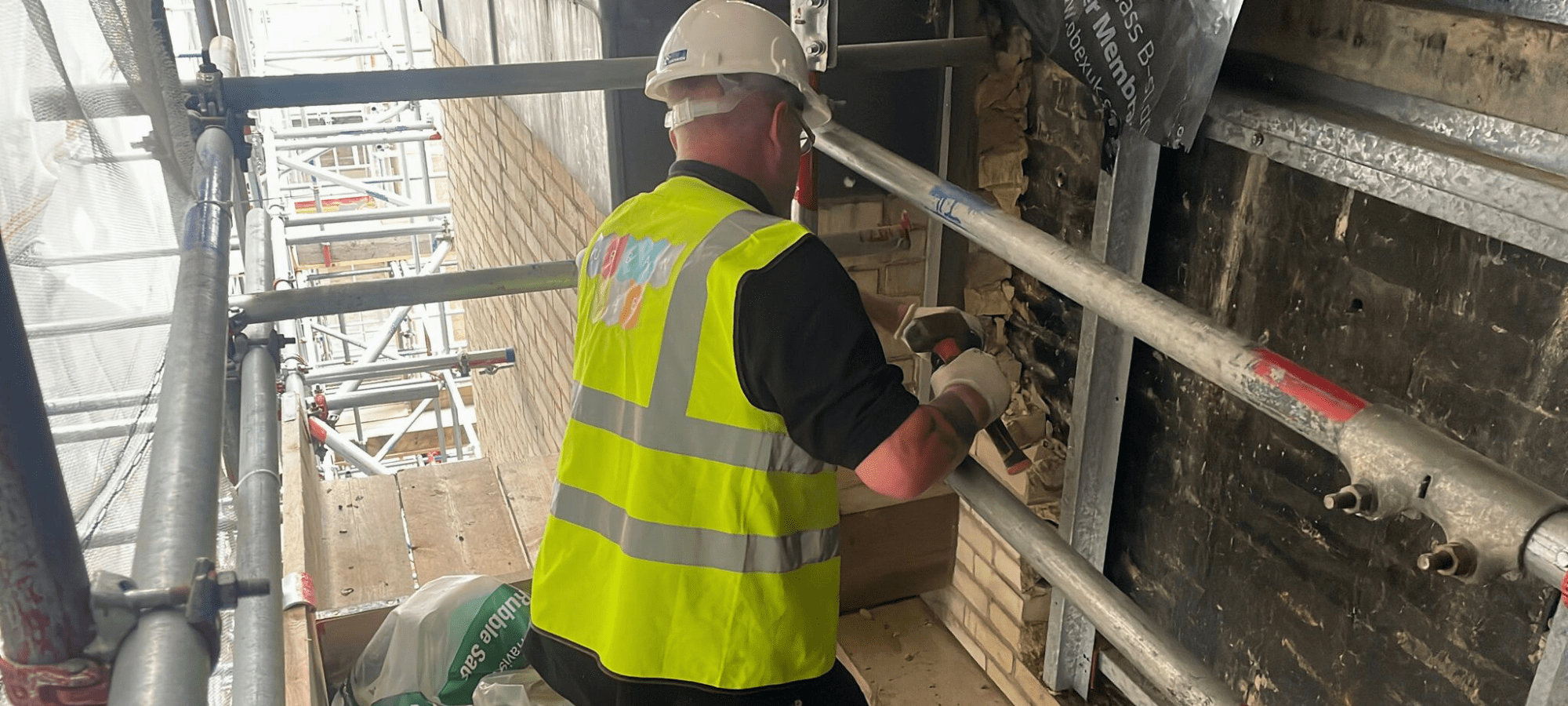 Urbanise team member in a high vis yellow jacket and hard hat hammering and working on the project