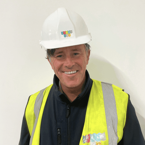 Headshot of Tommy smiling. He is wearing an Urbanise branded hard hat and hi-vis vest.