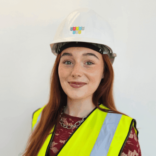 Headshot of Katie smiling. She is wearing an Urbanise branded hard hat and hi-vis vest.