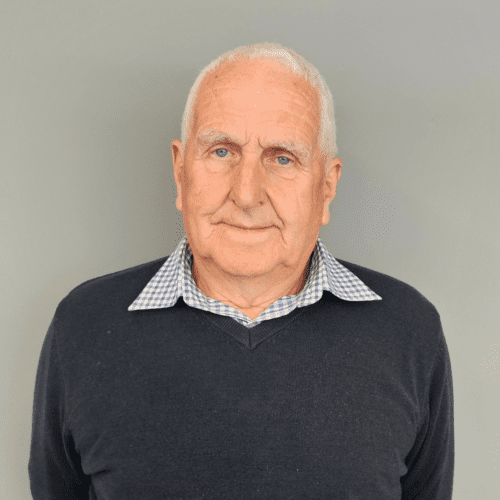 Headshot of Gwyn smiling. He is wearing a navy jumper over a navy and white chequered shirt.